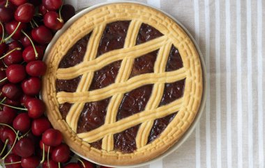 Lezzetli bir vişneli turta masada taze kirazların yanında duruyor..