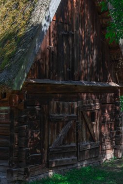 Ağaçlarla gölgelenmiş, sazdan çatılı ahşap bir bina..