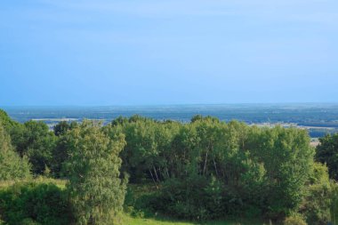 Bereketli ağaçlar ve yuvarlanan tepeler parlak bir gökyüzünün altında ufka doğru uzanır..
