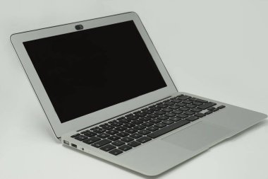 Siyah ekran ve beyaz zemin üzerinde siyah tuşlar olan küçük gümüş renkli hafif bir laptop.