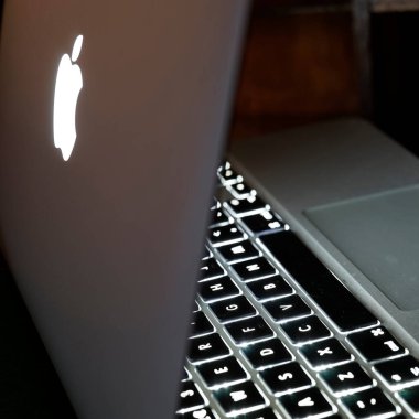 Itterbeck, Almanya - 3 Kasım 2022 Elma dizüstü bilgisayarının arka plandaki klavyesi. Bu eski Macbook havasının arkasında hala aydınlatılmış bir elma logosu var.