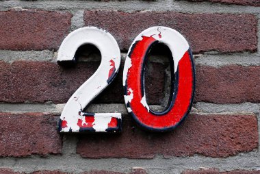 Number 20 in red  numbers on a brick wall. Half of the red paint is gone. The white is left. These kinds of house numbers were fashionable in the Netherlands for a long time