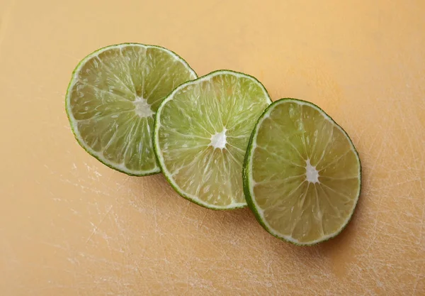 Persian lime fruit slices on an orange cutting board. Lime is a citrus fruit. This lime is a cross between key lime and lemon