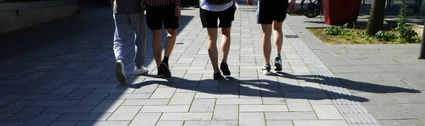 4人の男性の友人の足 彼らは広い通りを歩いている 3本の脚がある 石畳の上に影が見える — ストック写真