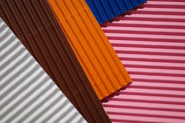 Horizontally and diagonally ribbed cardboard with the colors pink, white,  orange, brown, blue. Meant as background