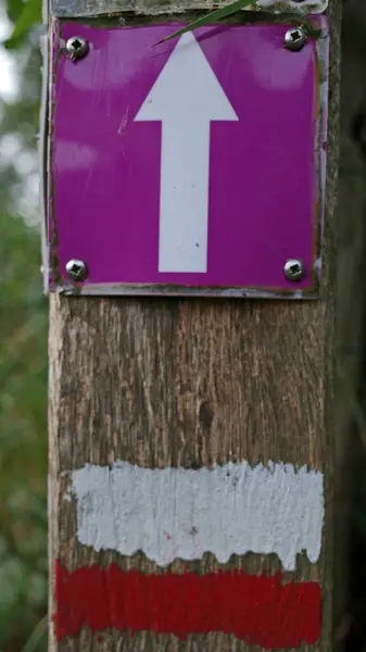 stock image Two markers on a post next to a path. A white arrow on a purple background for a local hiking trail and red and white stripes for a long-distance hike