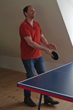 40 'lı yaşlarda yakışıklı bir adam gündelik kıyafetlerle masa tenisi oynar. Belli ki oyundan hoşlanıyor.