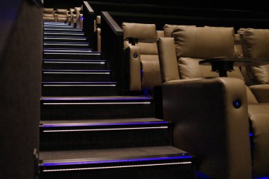 Lüks sandalyeler ve bir sinemanın oditoryumunda aydınlatılmış bir merdiven.