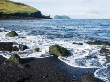 Heimaey Adası, Westman Adaları, İzlanda 'daki Klauf plajındaki siyah volkanik kumların üzerinde dalgalar yuvarlanıyor.