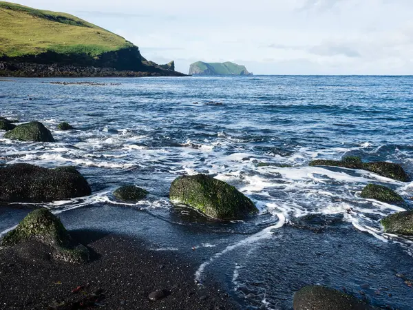 Heimaey Adası, Westman Adaları, İzlanda 'daki Klauf plajındaki siyah volkanik kumların üzerinde dalgalar yuvarlanıyor.