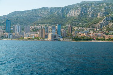 Monte Carlo kıyı şeridi. Arka planda dağlar ve kıyıya yakın binalar var.