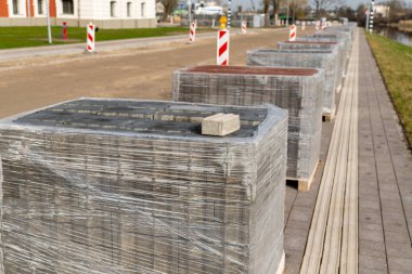 Bir sıra tuğla, su kenarındaki ahşap bir palette oturur ve gökyüzünün suya yansıdığı, bu arazi arazisindeki bir inşaat projesi potansiyelini gösteren resimsel bir sahne yaratır.