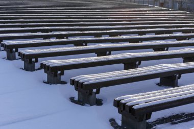 Açık havada izleyiciler için arka arkaya kar kaplı banklar, soğuk hava, sığ bir alan derinliği ile fotoğraflanmış, alçak bir bakış açısından, akşam ışığı