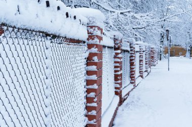 Kar yağışı sırasında farklı bir odak noktasıyla çekilmiş bir sokak boyunca bir çit, yol tozlu, bir bina ve bir yol kavşağı uzaklıktan görülebiliyor