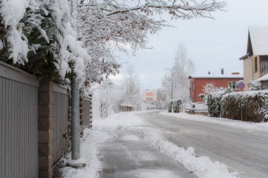Güneşli bir akşamda küçük bir Letonya kasabasının manzarası, ağaçlar, çalılar, çitler, yeşillikler, kar ve buz yığınları, farklı odak noktaları, farklı çerçeveler, kaldırımlar ve yollar, eski binalar.
