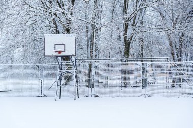 Karda serbest erişilebilir basketbol sahası, çitlerle çevrili, insan yok, hava koşulları kar, sokak topu sahası.