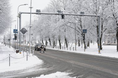 Bir yaya, yeşil trafik ışığında kar yağışı sırasında yaya geçidini geçer. Bir araba yayanın geçmesine izin vermek için durdu. Cadde tozla kaplı. Bir kuşun gözünden çekilmiş..