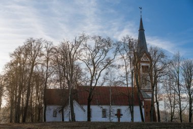 Ağaçlarla kaplı bir tarlanın ortasında küçük ve eski bir kırsal kilise, kulenin tepesinde bir horoz, Letonya 'da bir Lüteryen kilisesi, mezarlığın etrafında Krimulda kilisesi.