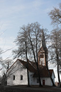 Ağaçlarla kaplı bir tarlanın ortasında küçük ve eski bir kırsal kilise, kulenin tepesinde bir horoz, Letonya 'da bir Lüteryen kilisesi, mezarlığın etrafında Krimulda kilisesi.