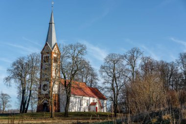 Ağaçlarla kaplı bir tarlanın ortasında küçük ve eski bir kırsal kilise, kulenin tepesinde bir horoz, Letonya 'da bir Lüteryen kilisesi, mezarlığın etrafında Krimulda kilisesi.