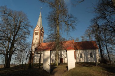 Ağaçlarla kaplı bir tarlanın ortasında küçük ve eski bir kırsal kilise, kulenin tepesinde bir horoz, Letonya 'da bir Lüteryen kilisesi, mezarlığın etrafında Krimulda kilisesi.