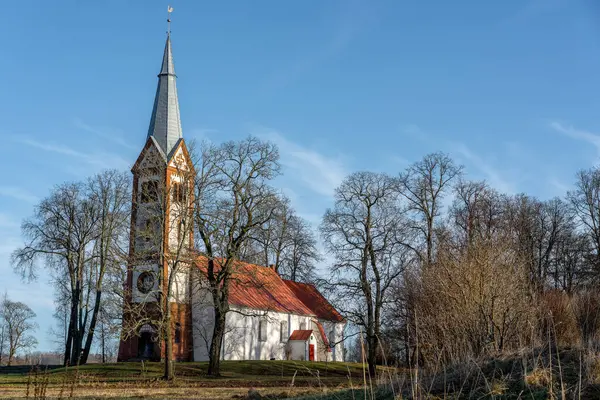 Ağaçlarla kaplı bir tarlanın ortasında küçük ve eski bir kırsal kilise, kulenin tepesinde bir horoz, Letonya 'da bir Lüteryen kilisesi, mezarlığın etrafında Krimulda kilisesi.