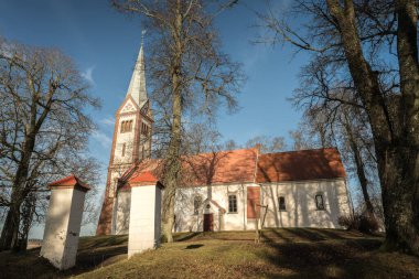 Ağaçlarla kaplı bir tarlanın ortasında küçük ve eski bir kırsal kilise, kulenin tepesinde bir horoz, Letonya 'da bir Lüteryen kilisesi, mezarlığın etrafında Krimulda kilisesi.