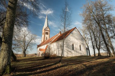 Ağaçlarla kaplı bir tarlanın ortasında küçük ve eski bir kırsal kilise, kulenin tepesinde bir horoz, Letonya 'da bir Lüteryen kilisesi, mezarlığın etrafında Krimulda kilisesi.