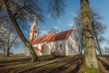 Ağaçlarla kaplı bir tarlanın ortasında küçük ve eski bir kırsal kilise, kulenin tepesinde bir horoz, Letonya 'da bir Lüteryen kilisesi, mezarlığın etrafında Krimulda kilisesi.