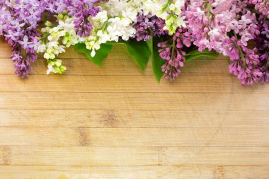 Eski ve çizilmiş bir tahta üzerinde çeşitli renklerde leylak çiçekleri. Yazıtlar ve nesneler için boş alanı var. Yüksek bir açıyla, geniş bir alan derinliğinde fotoğraflanmış.