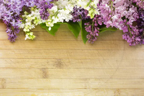 Eski ve çizilmiş bir tahta üzerinde çeşitli renklerde leylak çiçekleri. Yazıtlar ve nesneler için boş alanı var. Yüksek bir açıyla, geniş bir alan derinliğinde fotoğraflanmış.