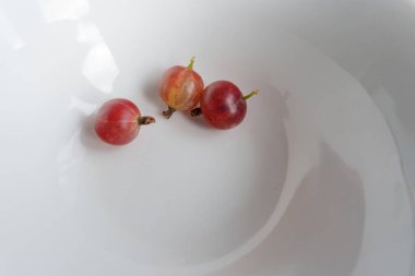 Beyaz bir kasede birkaç olgun bektaşi üzümü var. Bir dut ikiye bölünür ve eti ve tohumları ortaya çıkar. Arka plan temiz, beyaz bir kase.