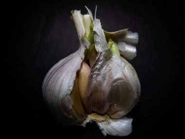 Koyu bir arka planda, kağıttan derili sarımsaklı bir ampulün ayrıntılı görüntüsü. Mutfak temalı içerik ve yemekteki tazeliği ve doğal malzemeleri vurgulamak için mükemmel..