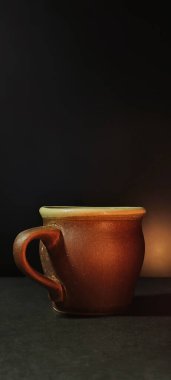 Güzel bir el yapımı seramik kupa, siyah arka planda, sanatsal ışıklandırmayla aydınlatılmış. Basitlik, zanaat ve günlük yaşam kavramlarını resmetmek için idealdir. Reklam ve sanatsal dekor için mükemmel bir görüntü..