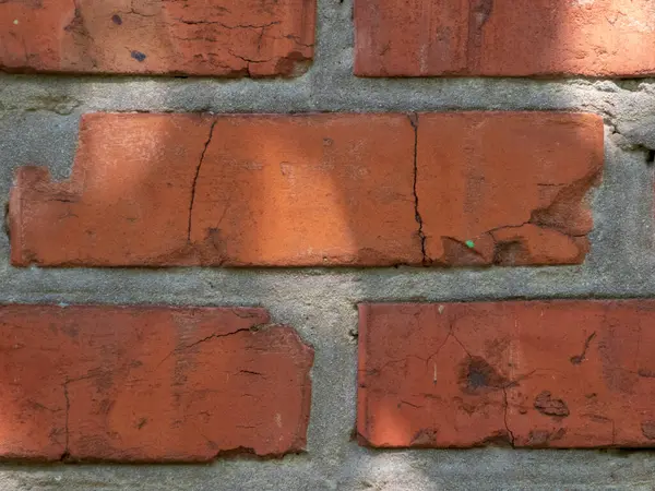Kırmızı tuğladan bir duvarın dokusunu ve kusurlarını gösteren detaylı bir yakın çekim fotoğrafı..