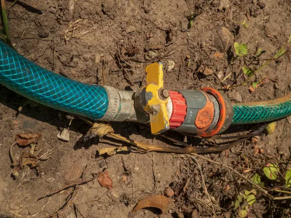 Kuru, gevşek toprak üzerinde sarı ve kırmızı kapaklı eski bir bahçe hortumu..