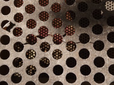 Arkaplanı bulanık olan hasarlı metal bir ızgaranın yakın çekimi.