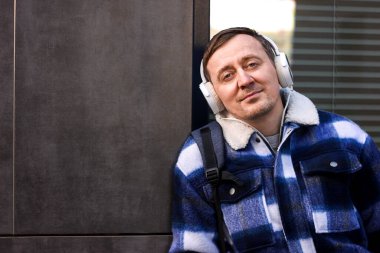 Bir adam duvarın yanında şık kıyafetler ve kulaklıklar takıyor, mesaj için boşluk kopyalıyor.