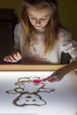 Güzel küçük kız ışık karesine kumla resim çiziyor, sanat terapisi, kum animasyonu, çocuklar için yaratıcı eğlence, seçici odaklanma.