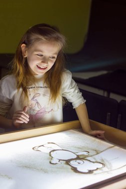 Güzel küçük kız ışık karesine kumla resim çiziyor, sanat terapisi, kum animasyonu, çocuklar için yaratıcı eğlence, seçici odaklanma.
