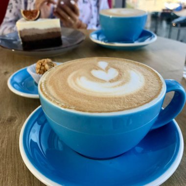 Kahve bardakları cappuccino, latte ve kakao, pastalar ve kafenin arka planında telefonu olan bir kızın elleri.