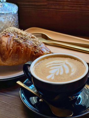 Bir fincan kahve, kruvasan ve ahşap yüzeyde altın çatal bıçak, koyu tonda geleneksel Fransız kahvaltı fotoğrafı.