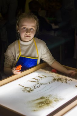 Güzel küçük kız ışık karesine kumla resim çiziyor, sanat terapisi, kum animasyonu, çocuklar için yaratıcı eğlence, seçici odaklanma.