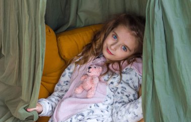 Rahat giysiler içindeki güzel küçük kız çocuk odasında elinde örülmüş oyuncak kigurumi ile oturuyor, seçici bir odaklanma.