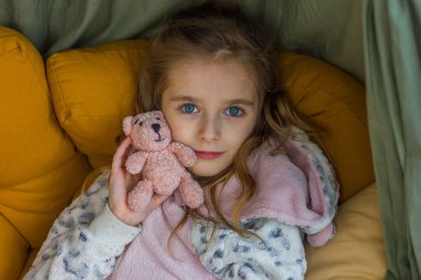 Rahat giysiler içindeki güzel küçük kız çocuk odasında elinde örülmüş oyuncak kigurumi ile oturuyor, seçici bir odaklanma.