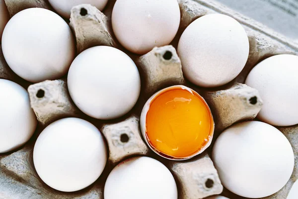 白い殻の卵と再生段ボールトレイに黄身と1つの壊れた卵のトップビュー 多様性個性健康食品という概念です 白い殻の卵の中で明るい黄色の黄身 — ストック写真