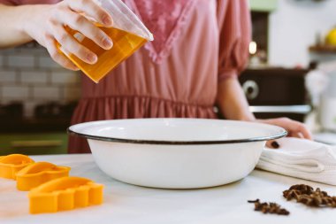 Ailede Noel kurabiyesi pişirmek. Noel kurabiyeleri için hamurunu hazırlıyor. Mutfağın arka planında parlak renkli çelenk ışıklarıyla süsleniyor.