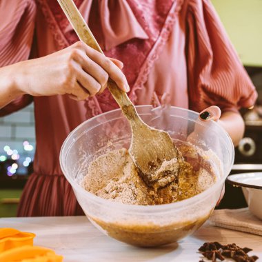 Ailede Noel kurabiyesi pişirmek. Noel kurabiyeleri için hamurunu hazırlıyor. Mutfağın arka planında parlak renkli çelenk ışıklarıyla süsleniyor.