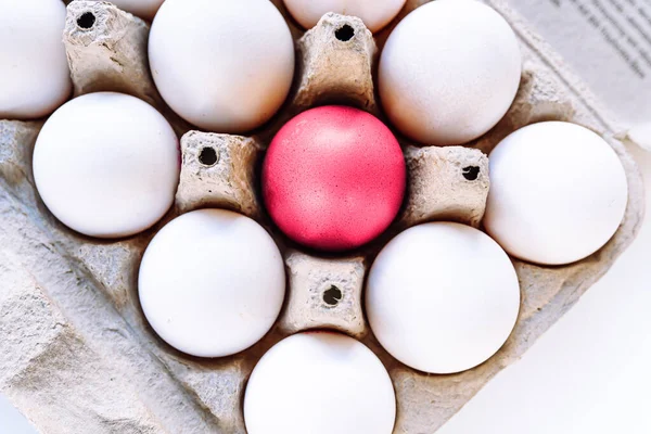 Cardboard tray filled with eggs, with brightly colored Viva Magenta eggs. Stand out from crowd, be brighter. Bright pink egg in a cardboard tray top view