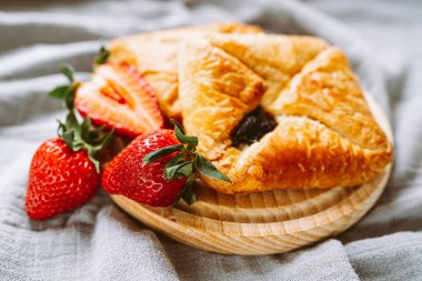 Marmelatla doldurulmuş tatlı poğaça zarfları. Çilekli tatlı pasta. Etrafa saçılmış çileklerle ahşap tahtayı keserken üfle.